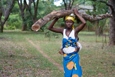 A woman with a baby carries a heavy log AND her baby